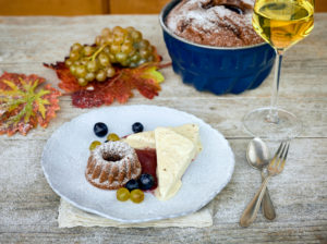 Sweet wine parfait with a small Guglhupf and wine berries on a white plate, white wine glass filled and baking pan, table with untreated table top Sweet wine parfait with a small Guglhupf and wine berries on a white plate, white wine glass filled and baking pan, table with untreated table top